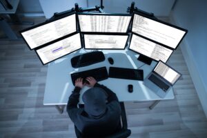 A hacker sat at a desk with six computer monitors and two keyboards. Cyber attacks were involved in many of the top 10 biggest data breaches in the UK.